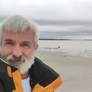 Capt. Paul Stancati, white beard, on a cloudy beach