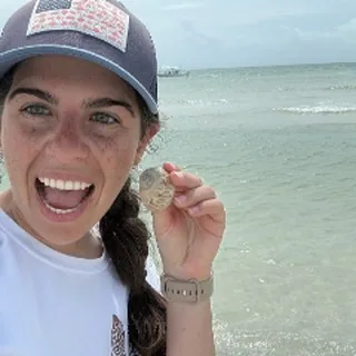 First Mate Taylor holding up a shell and laughing at the beach