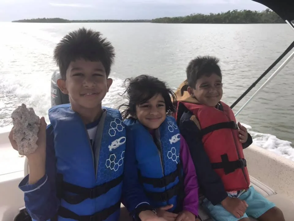 Three kids in life jackets on the boat, the oldest holding up a find