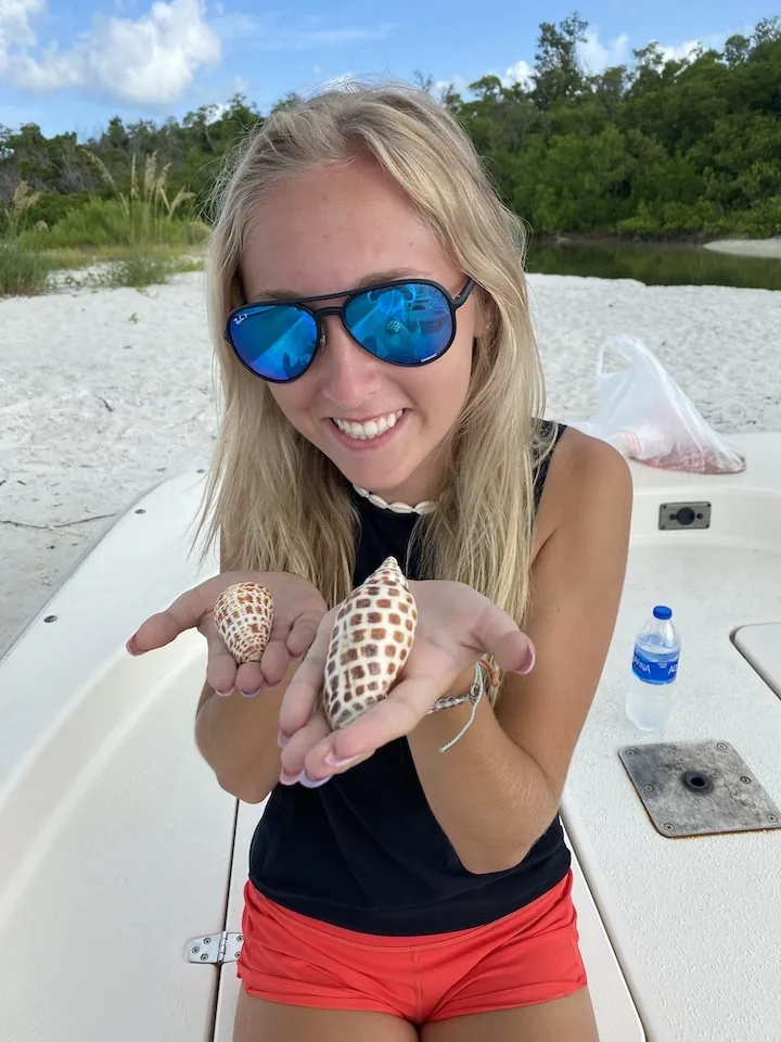 A guest on the boat holds up two spotted shells, one in each palm